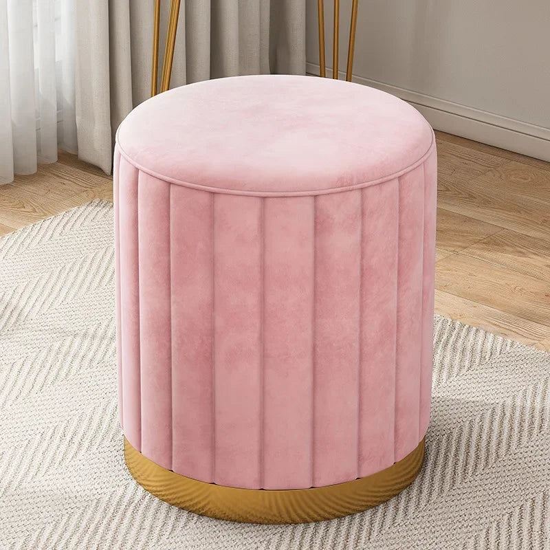 Vue légèrement en plongée du pouf rose en velours avec assise rembourrée, coutures verticales et base dorée.