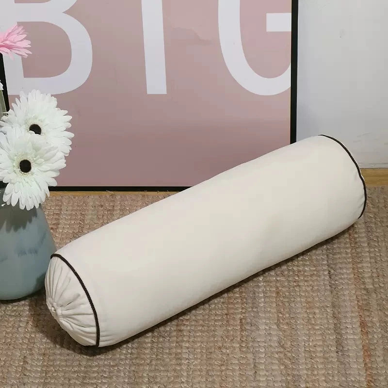 1. Coussin cylindrique blanc crème en velours avec extrémités froncées et passepoil foncé.