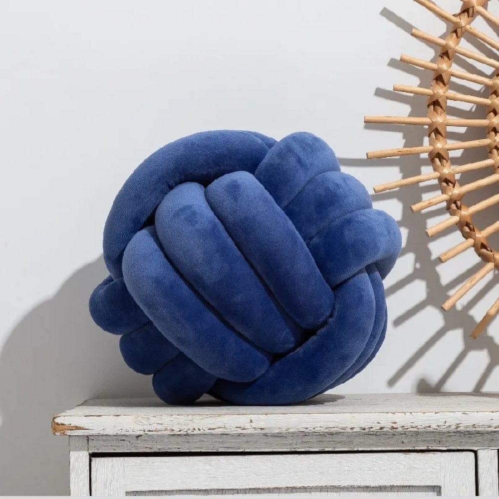 Coussin décoratif en velours bleu en forme de nœud, posé sur une table en bois, avec un décor mural en