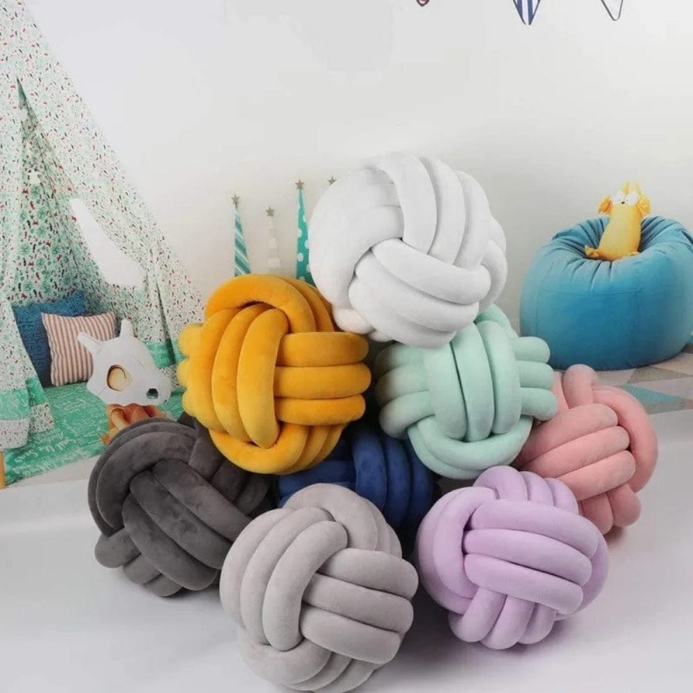Coussins décoratifs en forme de nœud, aux couleurs pastel, posés sur un sol clair dans un espace cosy