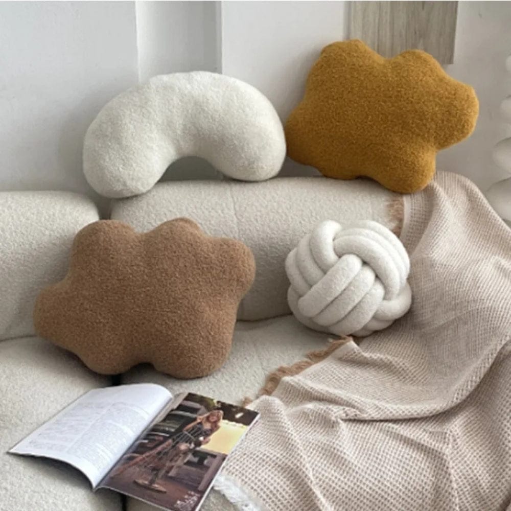 Quatre coussins décoratifs aux formes organiques, en laine, sur un canapé beige avec une couverture en tricot