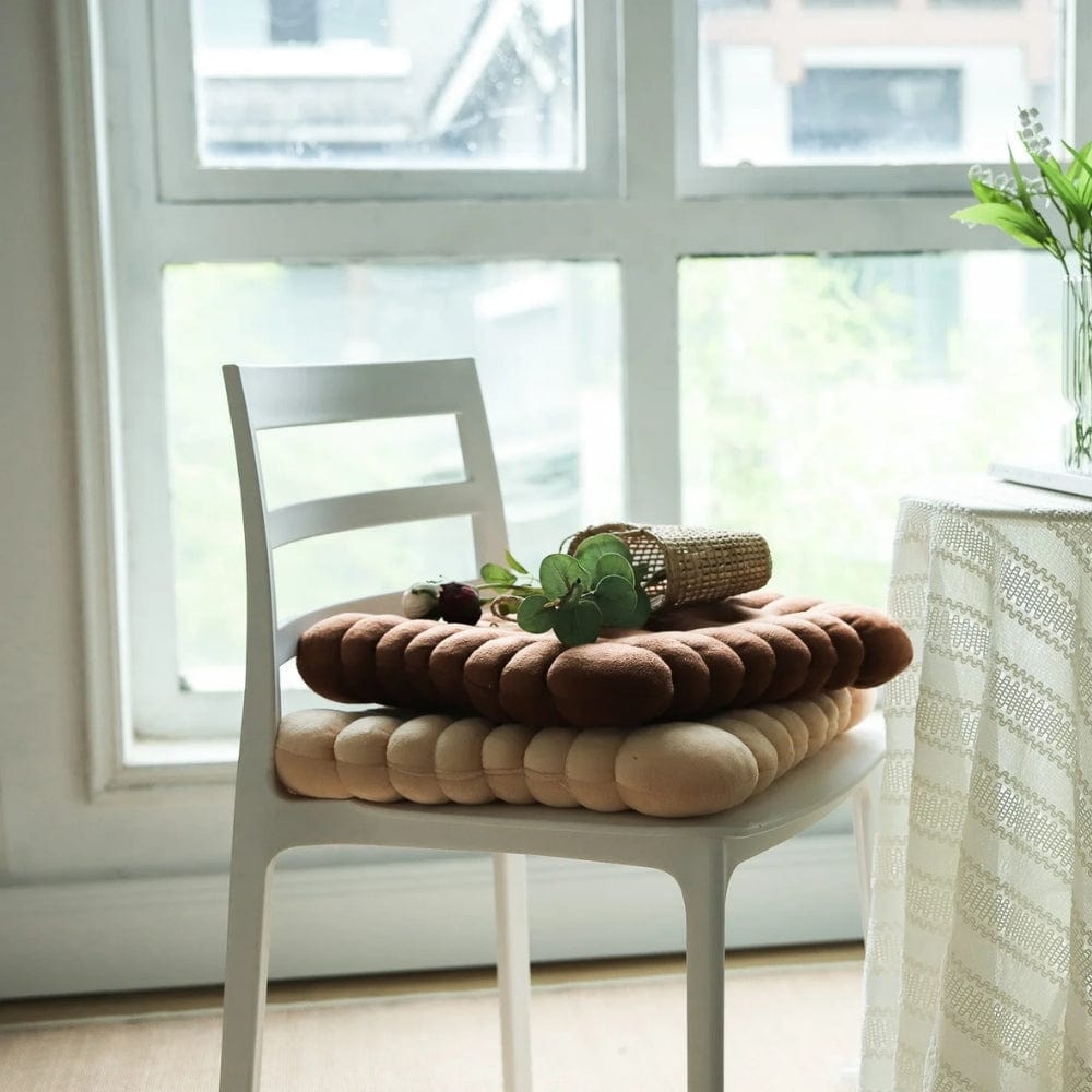 Coussins de chaise design aux teintes marron et beige, disposés sur une chaise blanche dans un intérieur lumineux
