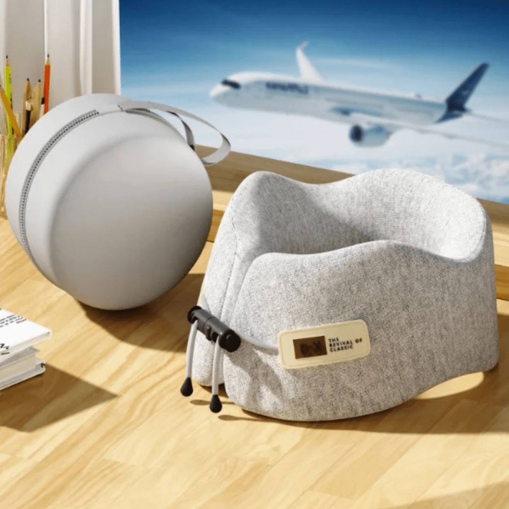 Coussin de cou en tissu gris, posé sur un bureau en bois, avec un design ergonomique pour le voyage