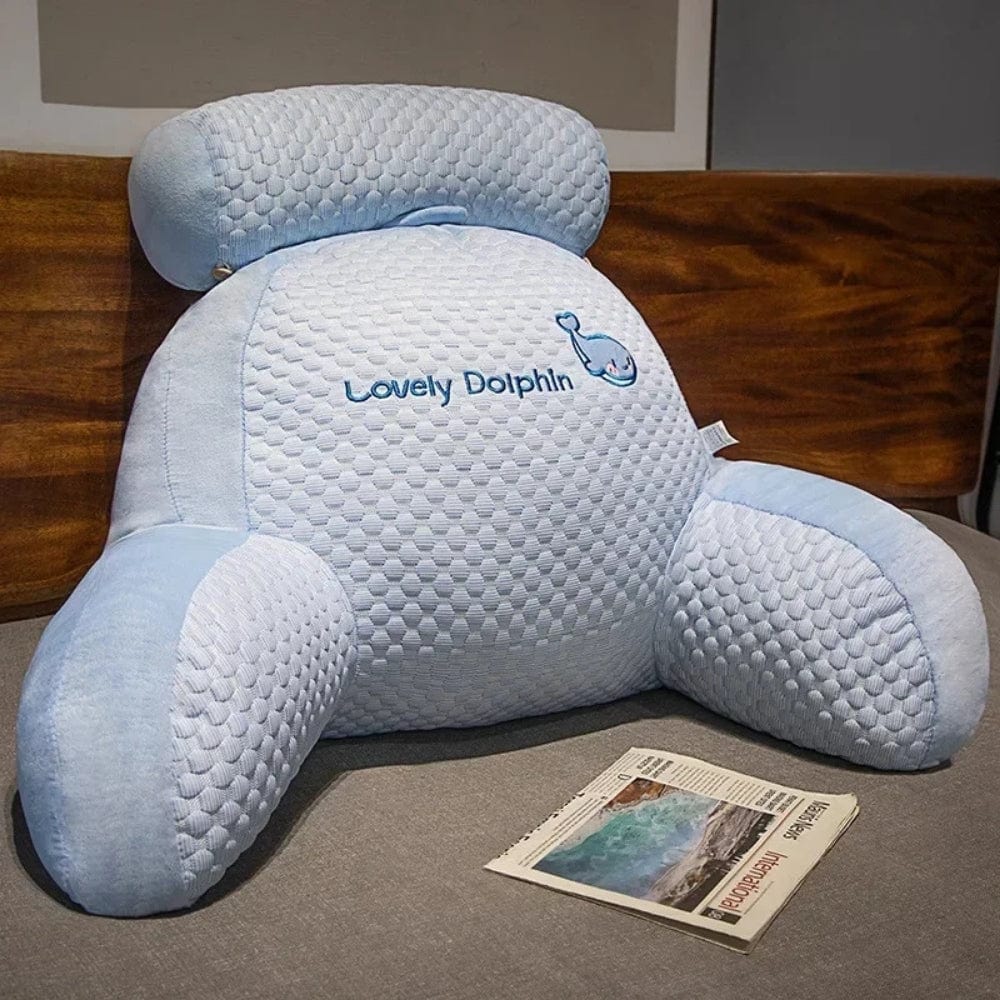 Coussin de lecture bleu clair en forme de dauphin, posé sur un lit avec un magazine à côté