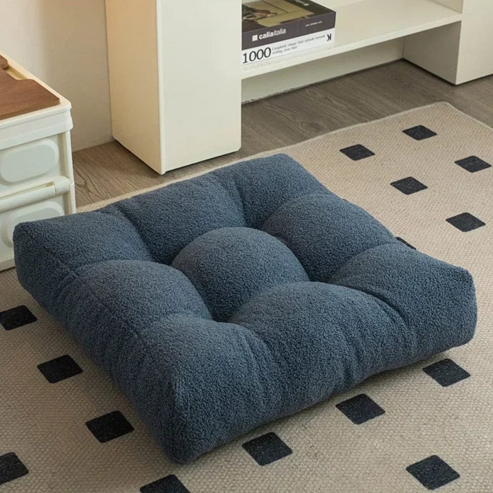 Coussin de sol en velours bleu foncé, posé sur un tapis beige à motifs carrés dans un salon moderne