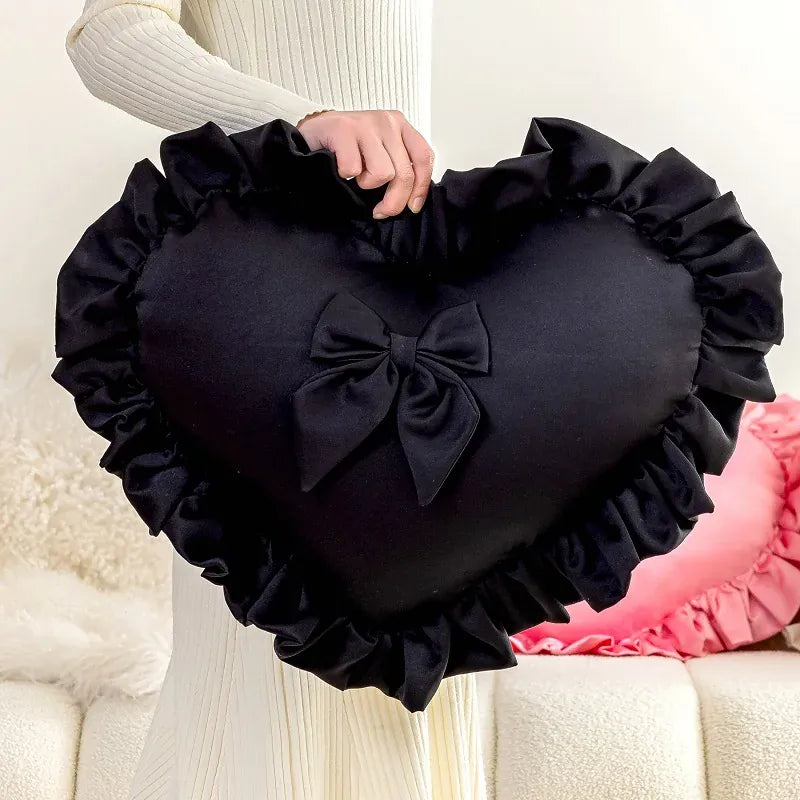 Coussin décoratif en forme de cœur noir avec volants et nœud, posé dans un salon élégant