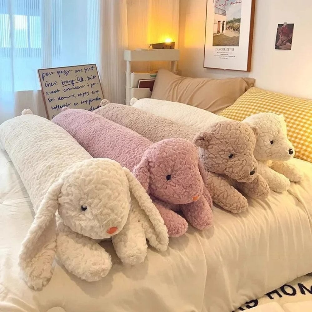 Coussins longs en peluche aux couleurs pastel, posés sur un lit avec des draps clairs et un décor chaleureux
