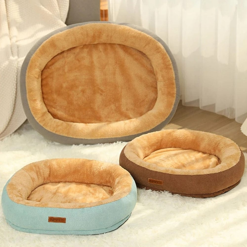 Coussins pour chat en forme ovale, en tissu doux beige et bleu, posés sur un tapis moelleux dans un salon