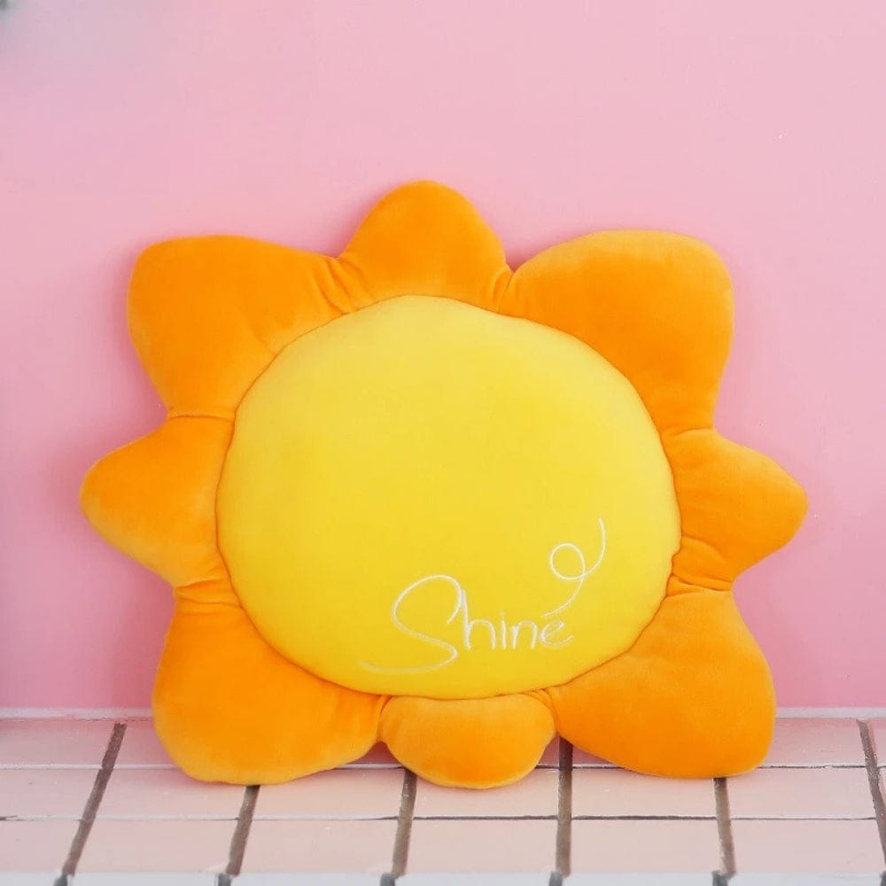 Coussin décoratif en forme de soleil, jaune et orange, posé sur un fond rose, idéal pour un canapé
