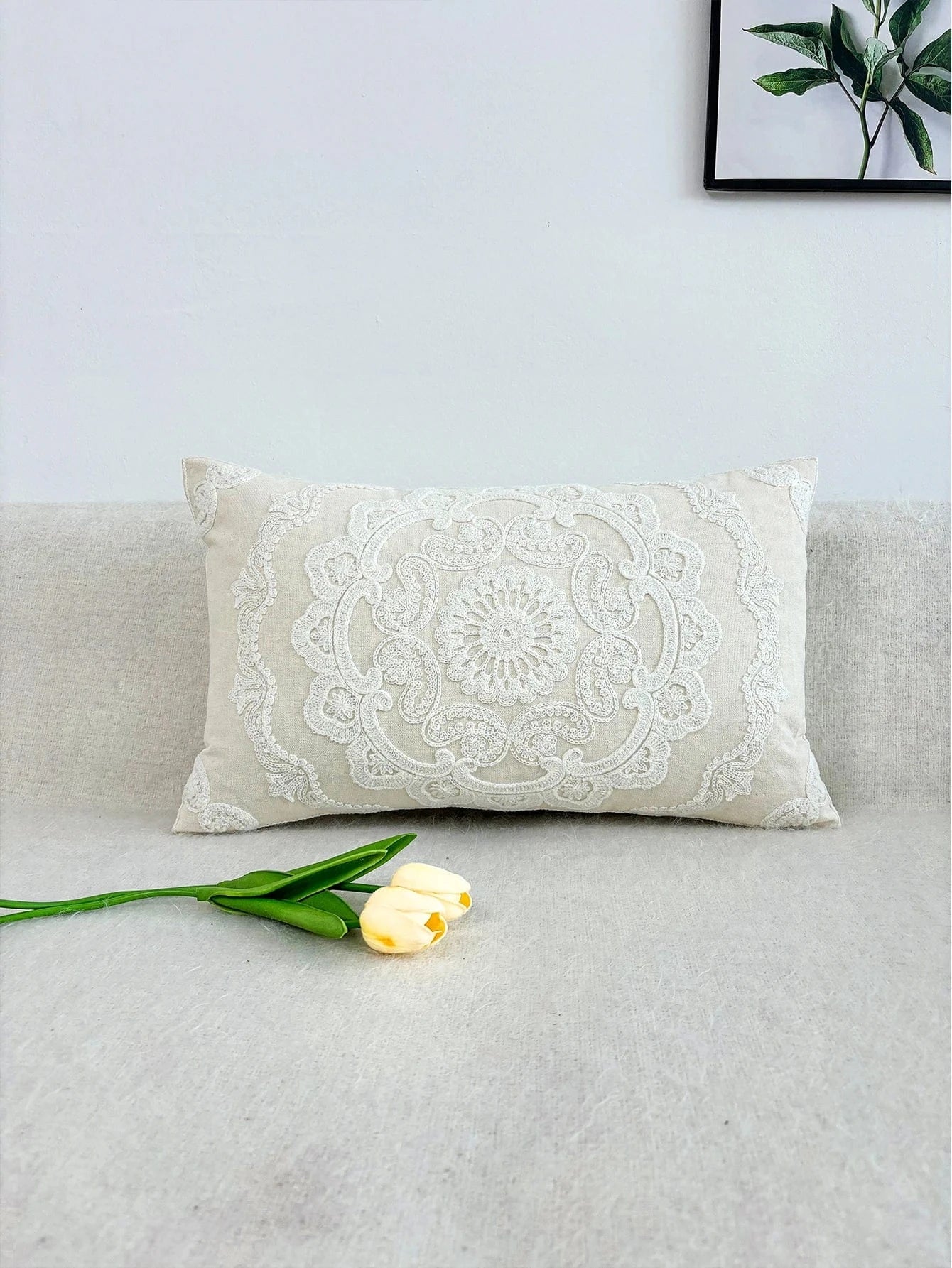 Coussin décoratif beige brodé sur un canapé, avec des motifs floraux et une texture douce