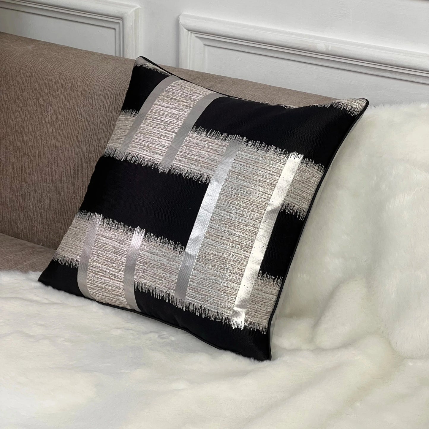 Coussin déco noir et argent avec motifs géométriques, posé sur un canapé en tissu beige, ajoutant une touche moderne