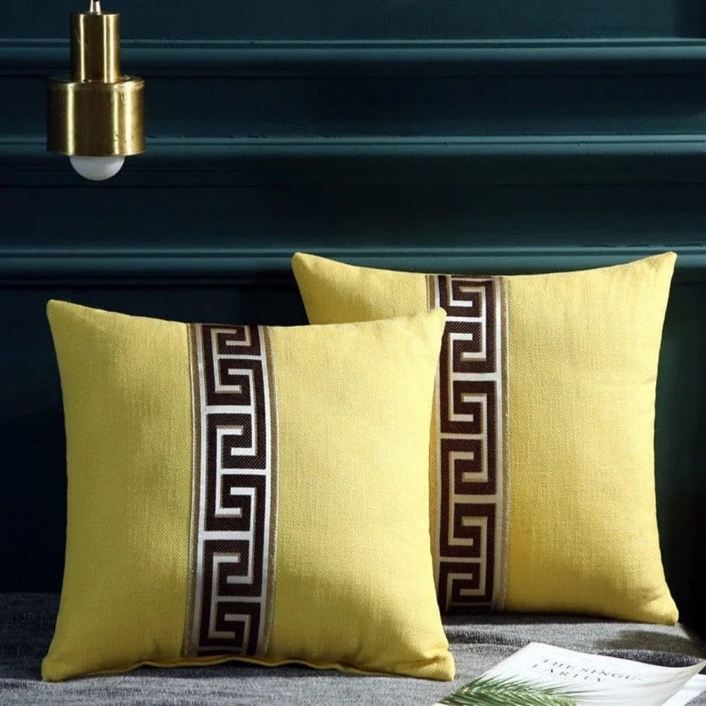 Deux coussins décoratifs jaunes avec un motif géométrique marron, posés sur un canapé gris dans un salon
