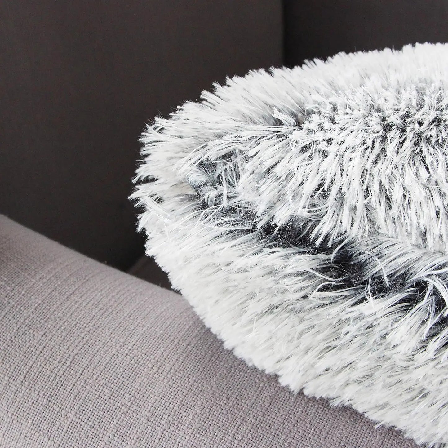 Coussin décoratif en fausse fourrure grise et blanche posé sur un canapé en tissu beige