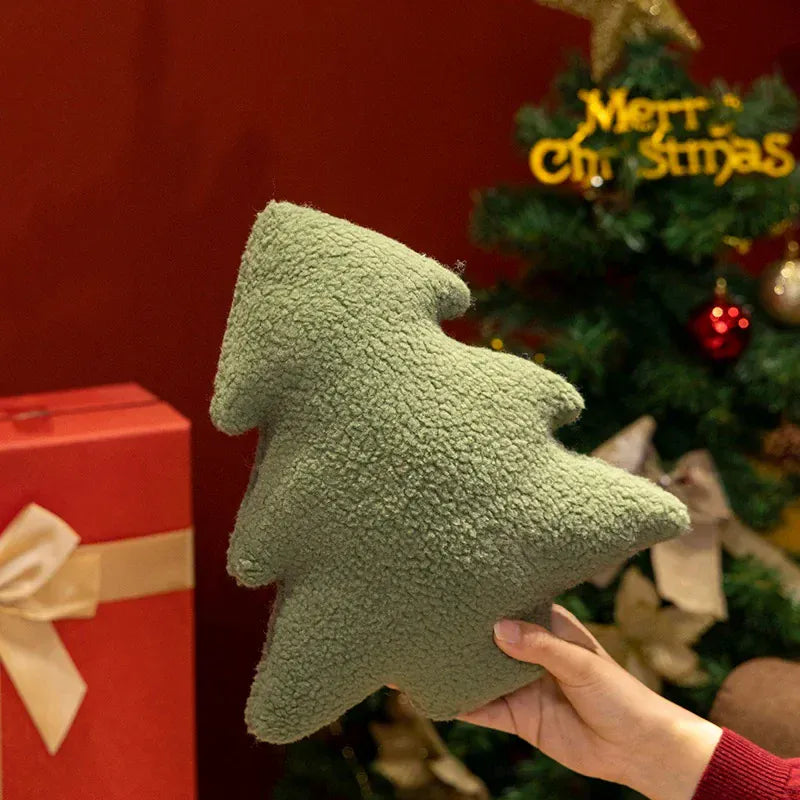 Coussin en forme de sapin de Noël vert en matière douce, posé devant un sapin décoré et des cadeaux