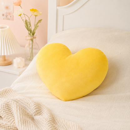 Coussin cœur jaune moelleux posé sur un lit beige dans une chambre douce et lumineuse.