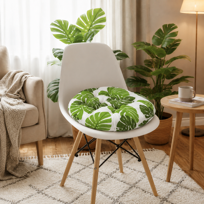 Coussin de chaise rond à motif feuilles vertes posé sur une chaise blanche dans un intérieur chaleureux et lumineux.