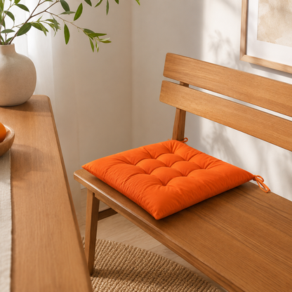 Coussin de chaise orange capitonné posé sur un banc en bois dans un intérieur lumineux.