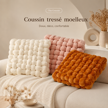 Coussins tressés ivoire, rose poudré et orange disposés sur un canapé beige.