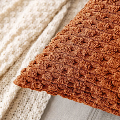 Détail rapproché d’un angle de housse de coussin terracotta posé sur un plaid beige.