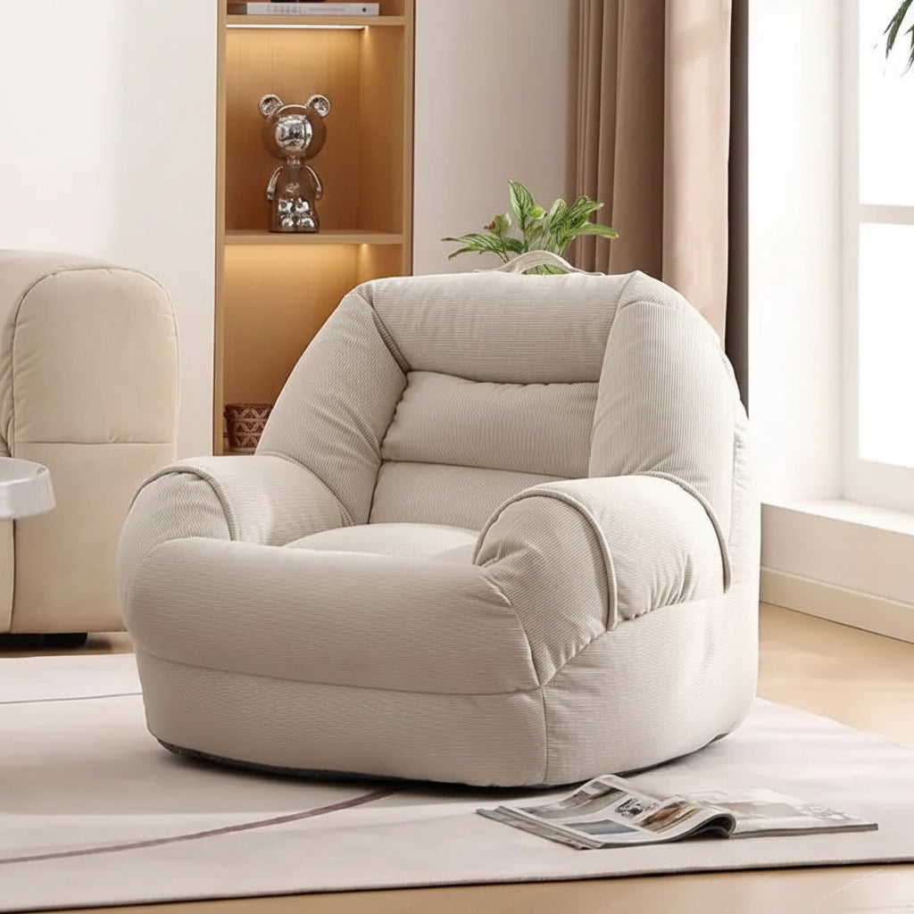 Fauteuil pouf en velours côtelé crème, vu de trois quarts, avec dossier rembourré et accoudoirs arrondis.