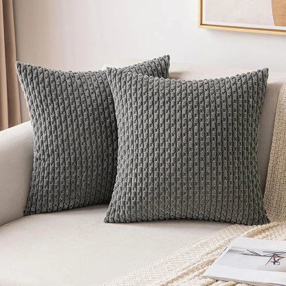Deux housses de coussin grises à texture côtelée disposées sur un canapé beige.