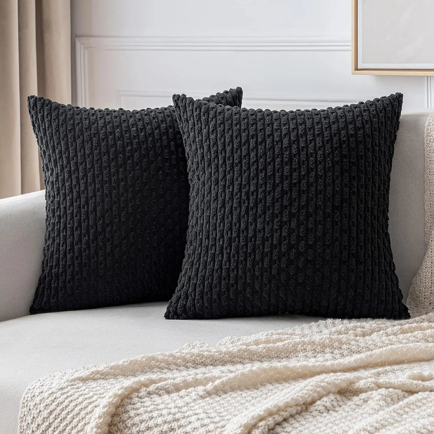 Deux housses de coussin noires à texture côtelée disposées sur un canapé beige.