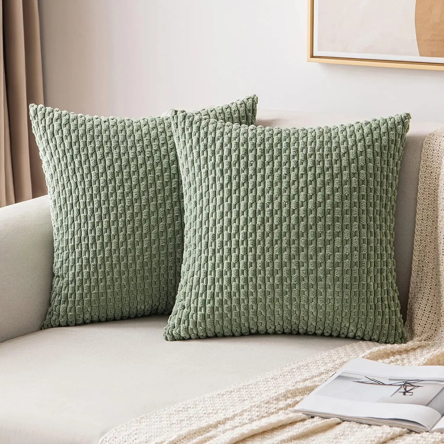 Deux housses de coussin vert sauge à texture côtelée présentées sur un canapé clair.