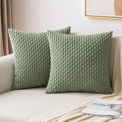 Deux housses de coussin vert sauge à texture côtelée présentées sur un canapé clair.