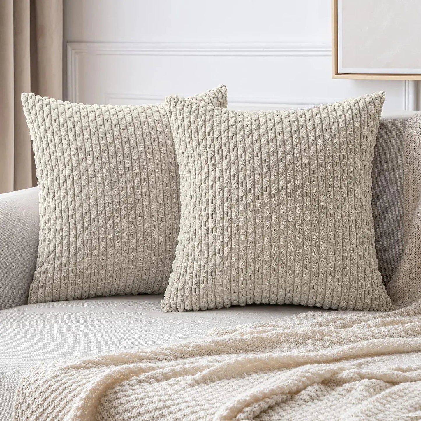 Deux housses de coussin beiges à relief côtelé présentées sur un canapé avec un plaid assorti.