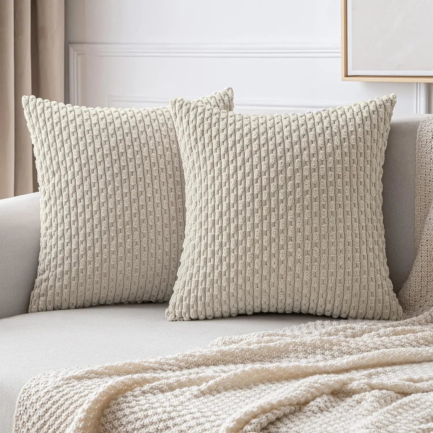 Deux housses de coussin beiges à relief côtelé présentées sur un canapé avec un plaid assorti.