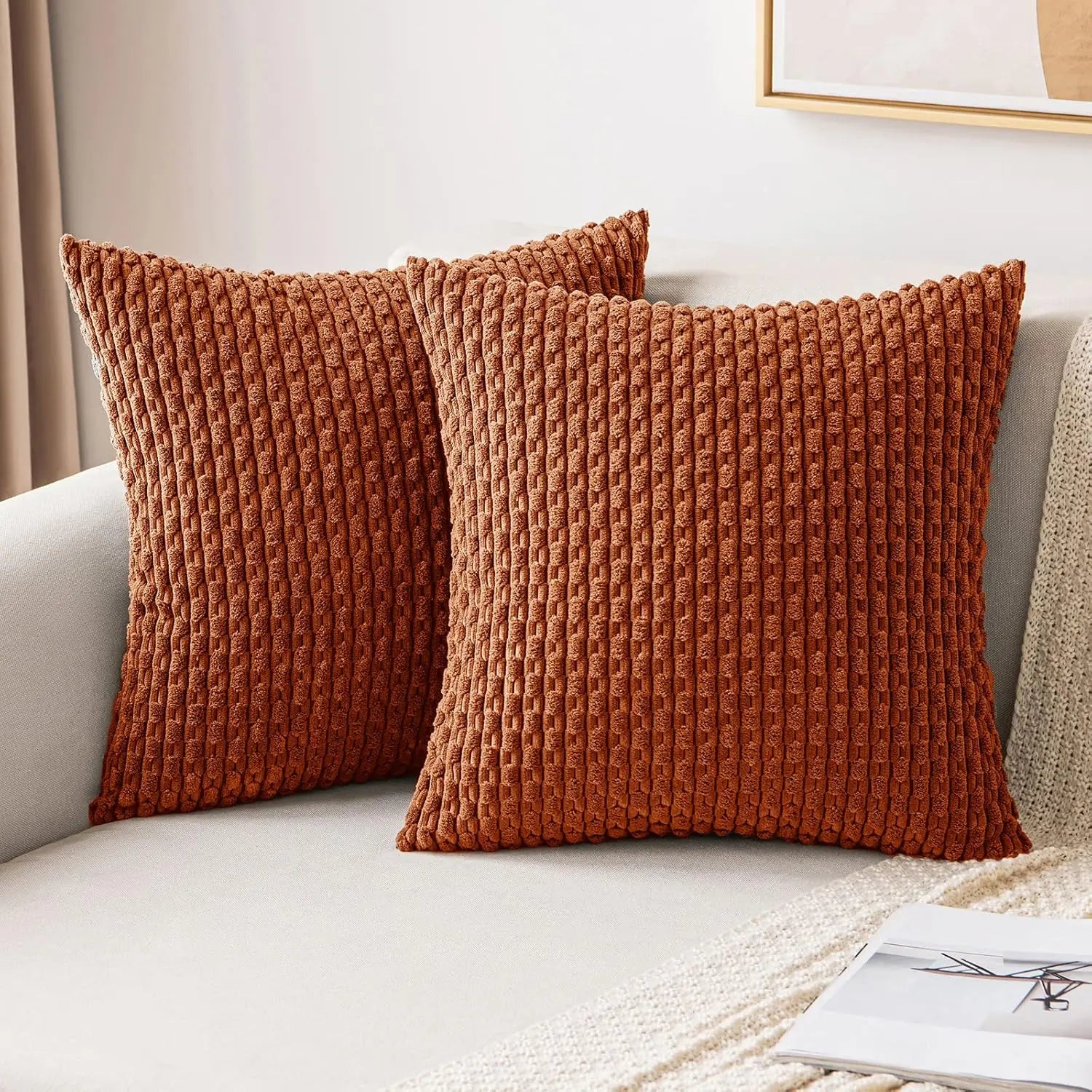 Deux housses de coussin terracotta à relief côtelé disposées sur un canapé beige.