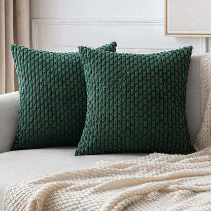 Deux housses de coussin vert forêt à texture côtelée disposées sur un canapé clair.