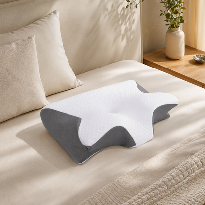 Oreiller cervical ergonomique blanc et gris présenté sur un lit dans une chambre moderne et apaisante.