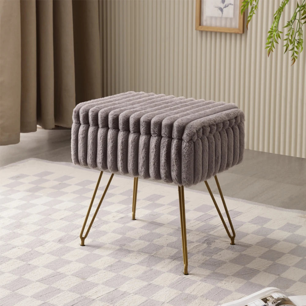 Pouf coffre gris en fausse fourrure à bandes en relief, avec couvercle fermé et pieds dorés, sur un tapis à motifs.