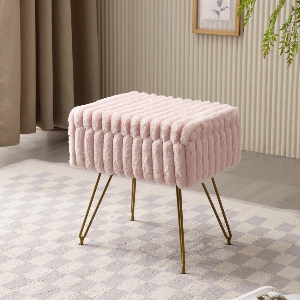 Pouf coffre rose en fausse fourrure à bandes en relief et pieds dorés, posé sur un tapis à motifs.