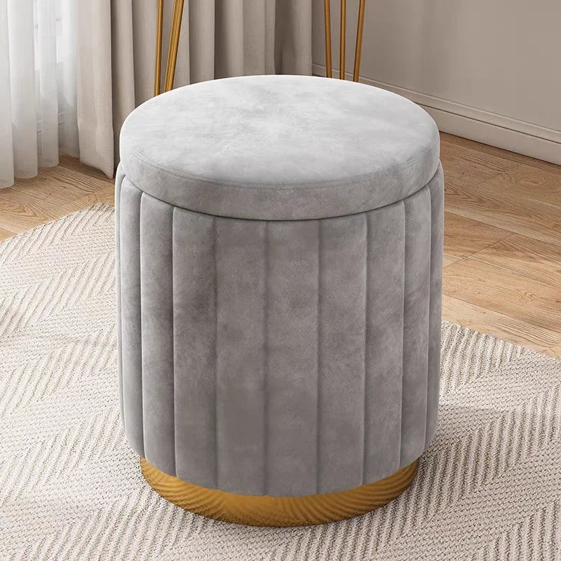 Vue légèrement en plongée du pouf gris en velours montrant son assise ronde, ses coutures verticales et sa base dorée.