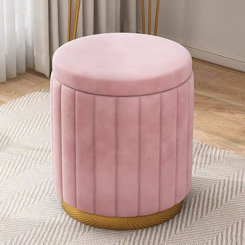 Pouf rond en velours rose avec coutures verticales, assise rembourrée et base dorée, sur un tapis clair.