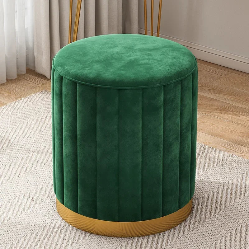 Pouf rond en velours vert avec coutures verticales, assise rembourrée et base dorée, sur un tapis clair.