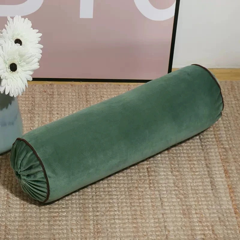 Coussin cylindrique vert en velours avec extrémités froncées et passepoil foncé.