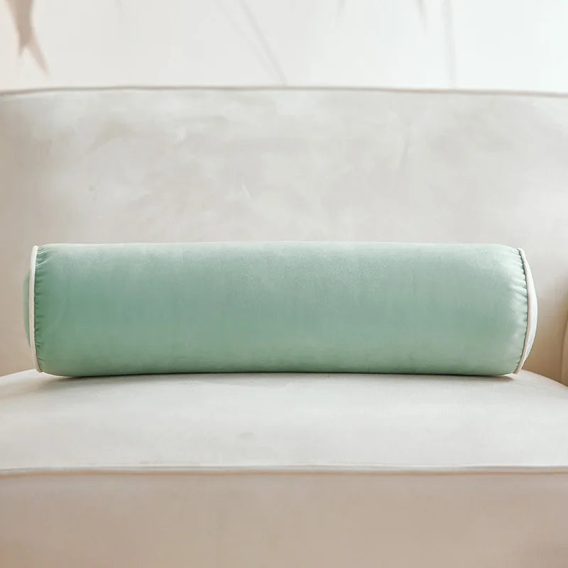 Coussin cylindrique vert sauge en velours posé sur un canapé crème.