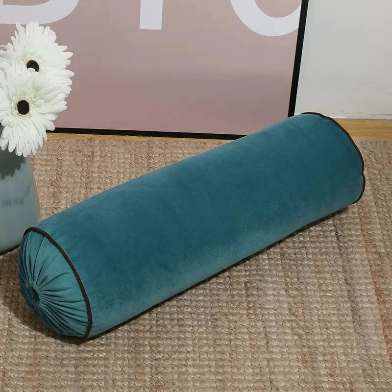 Coussin cylindrique bleu pétrole en velours avec extrémités froncées et passepoil foncé.