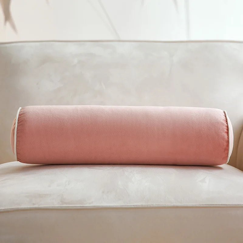 Coussin cylindrique rose poudré en velours posé sur un canapé crème.