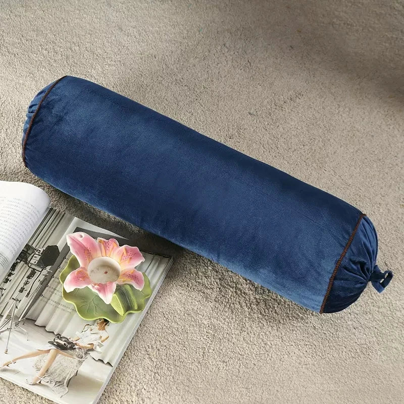 Coussin cylindrique bleu marine en velours posé près d’un magazine.
