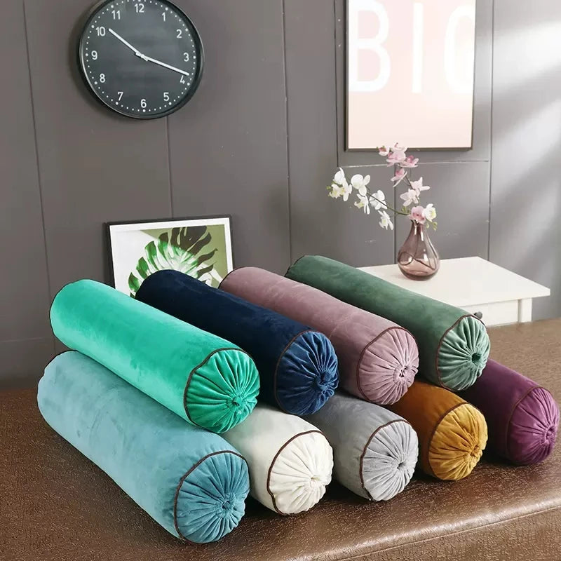 Ensemble de coussins cylindriques en velours de différentes couleurs, avec extrémités froncées et passepoil foncé.