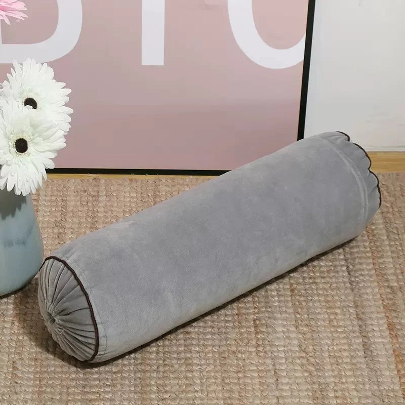 Coussin cylindrique gris en velours avec extrémités froncées et passepoil foncé.