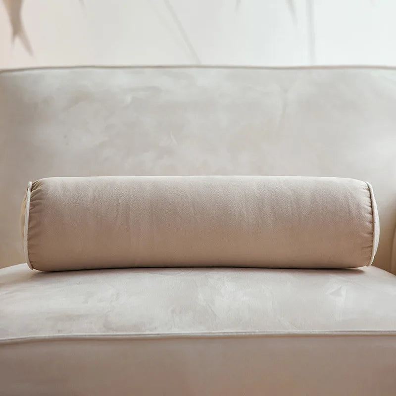 Coussin cylindrique beige en velours posé sur un canapé crème.