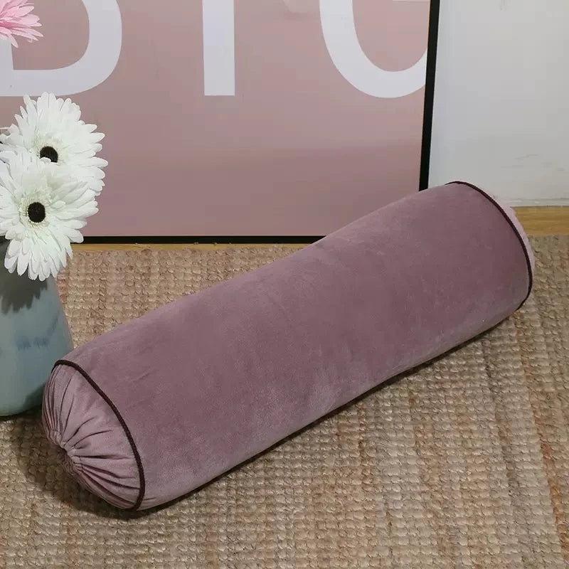Coussin cylindrique mauve en velours avec extrémités froncées et passepoil foncé.