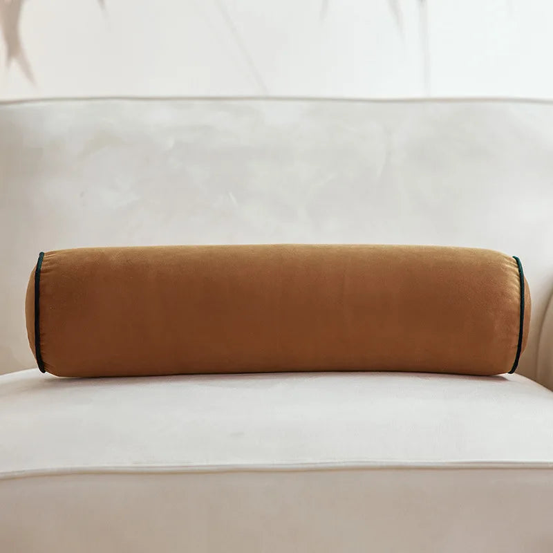 Coussin cylindrique camel en velours posé sur un canapé crème.