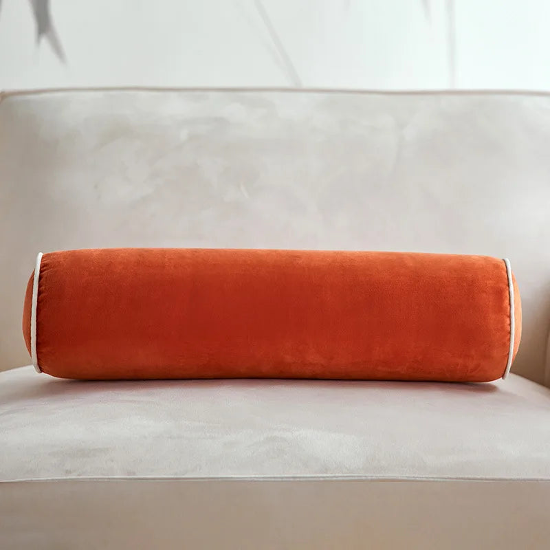 Coussin cylindrique orange terracotta en velours posé sur un canapé crème.