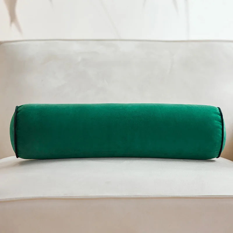 Coussin cylindrique vert foncé en velours posé sur un canapé crème.